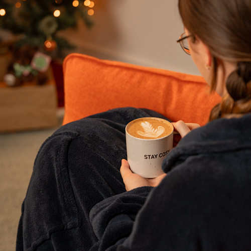 Lady sitting on a sofa with a Cinnamon Maple Latte next to a Christmas tree