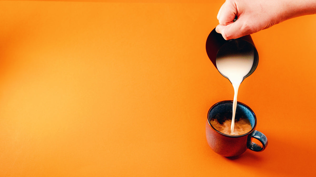 A jug of milk being poured into a cup of black coffee