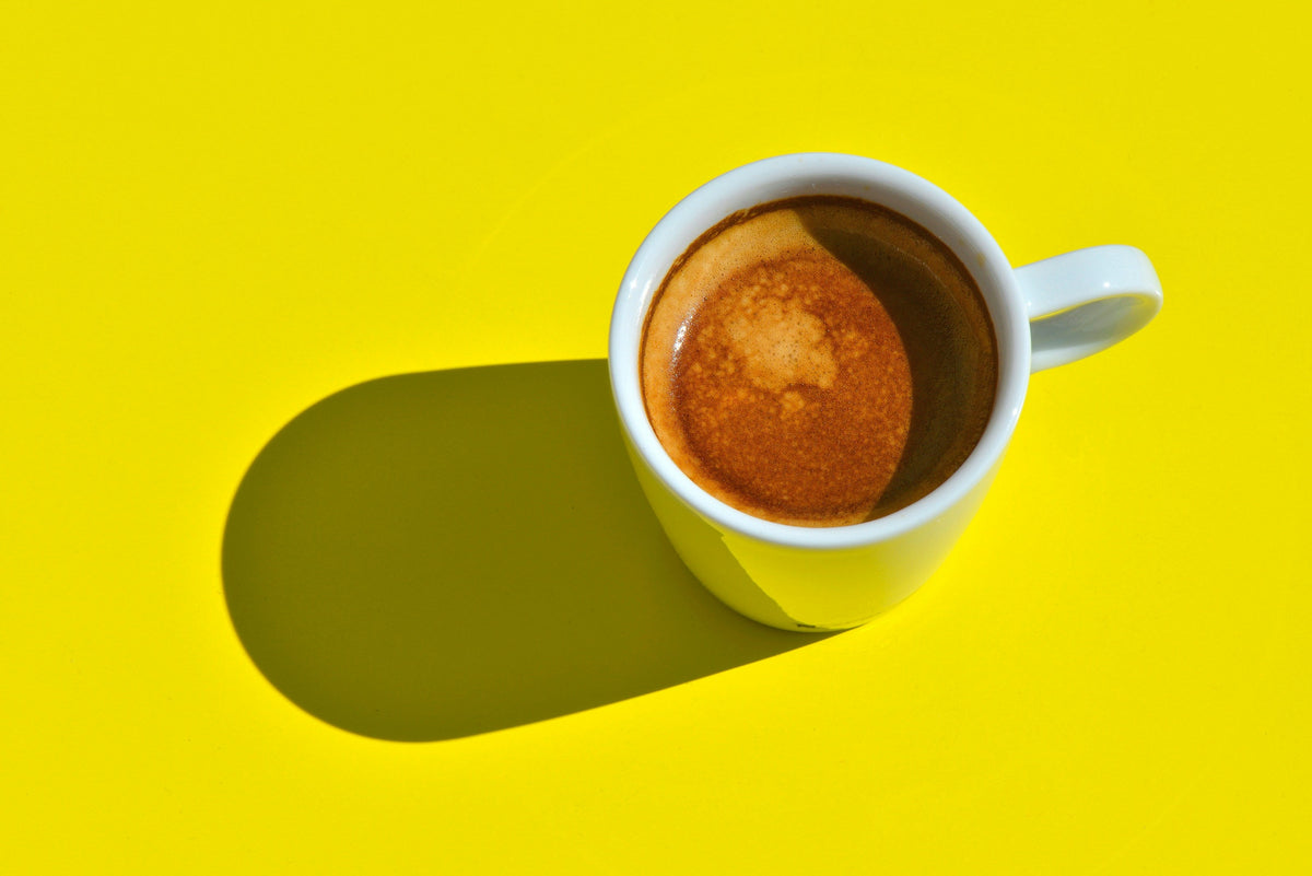 A cup of coffee with shadow on a bright yellow background