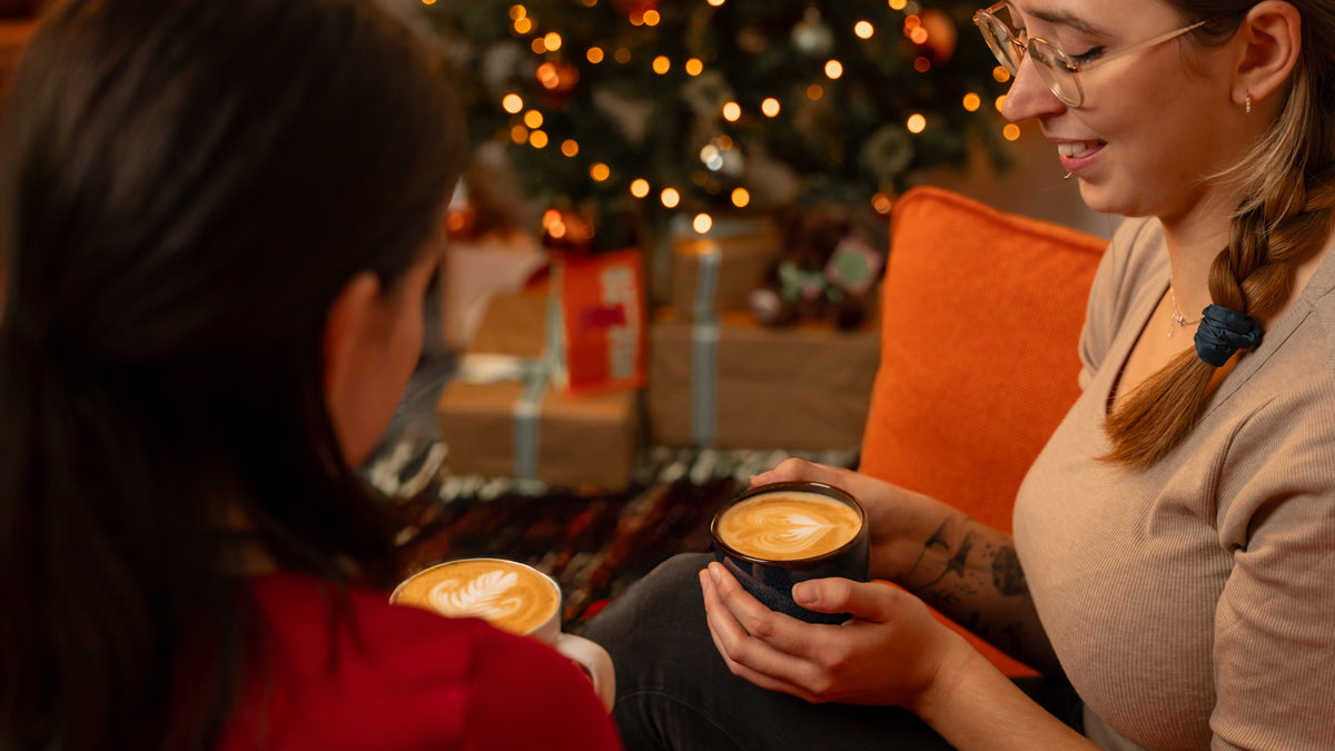 Two ladies enjoying festive coffee next to a Christmas tree 