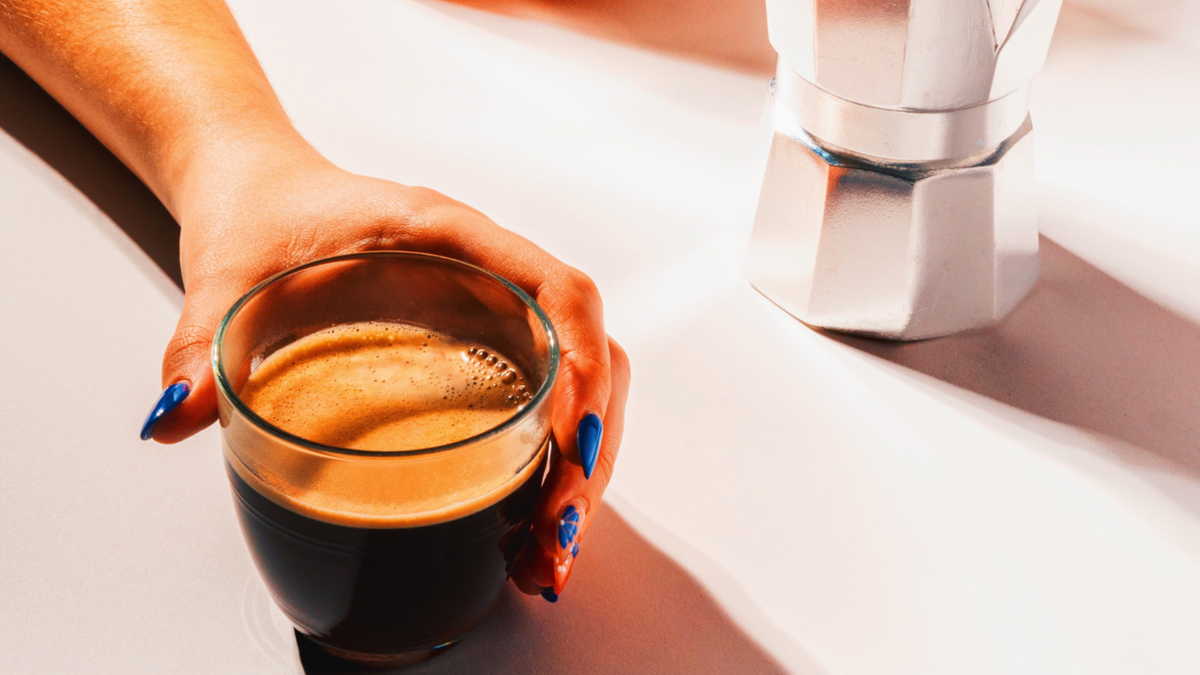 A glass of espresso coffee, next to a Moka pot 